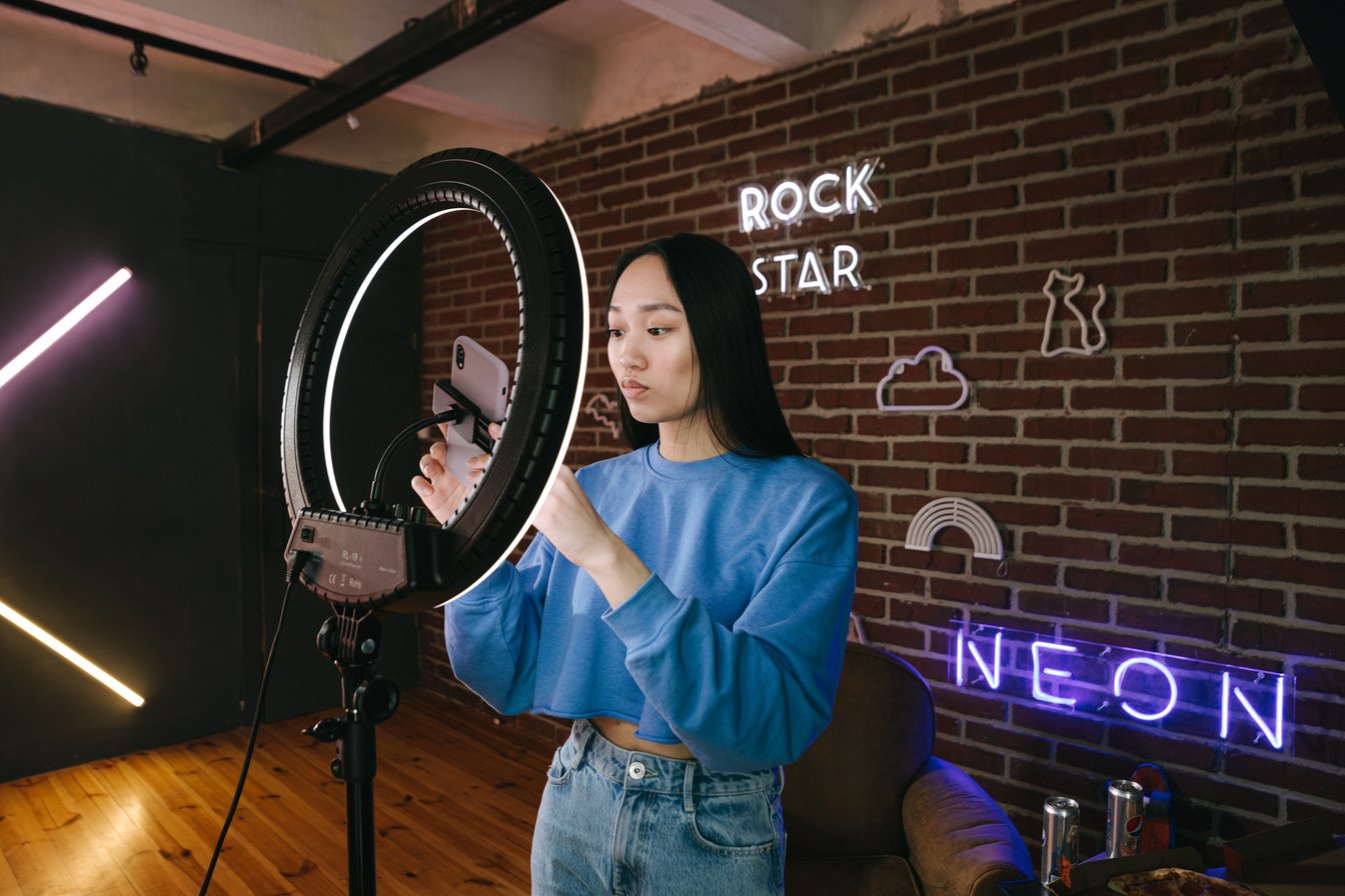 A Woman Using Her Phone while Attached on a Ring Light